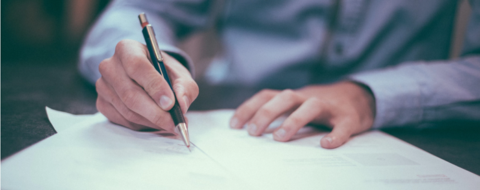 hands holding a pen and signing documents